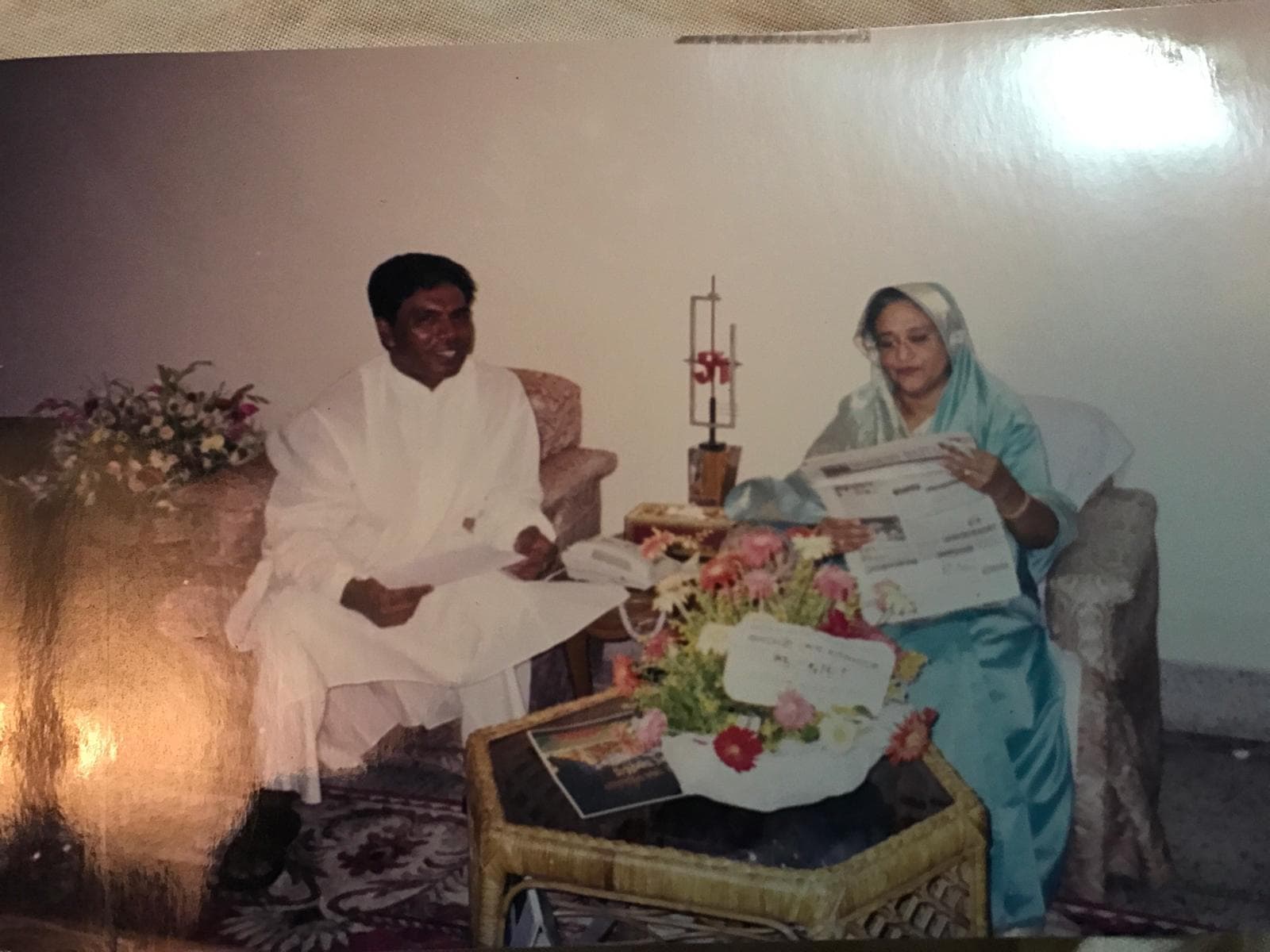 Sheikh Hasina reading a newspaper during a relaxed indoor conversation with a community representative